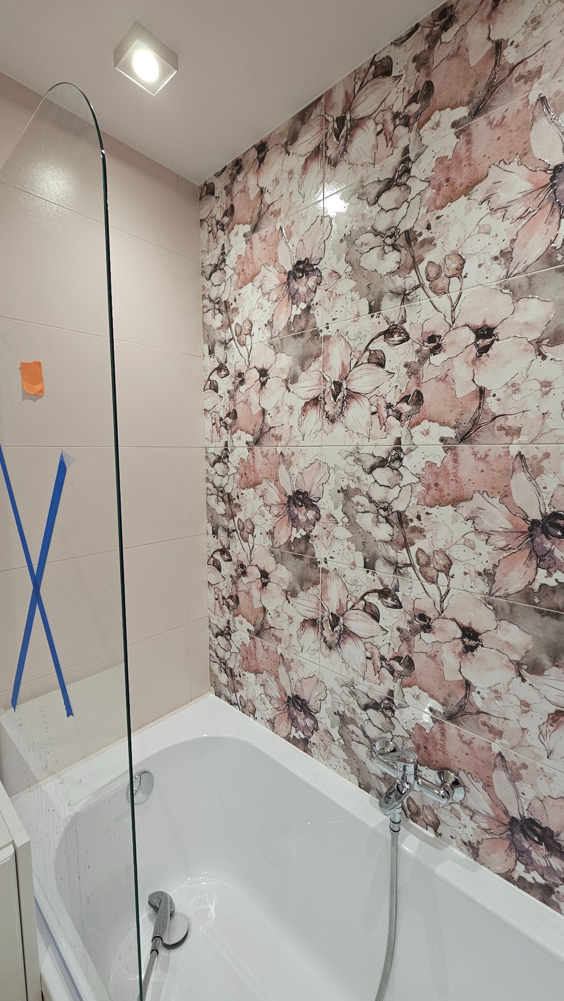 Wykończona łazienka z wanną, szklanym parawanem i płytkami w kwiatowy wzór. Na szklanym parawanie widoczne taśmy zabezpieczające.