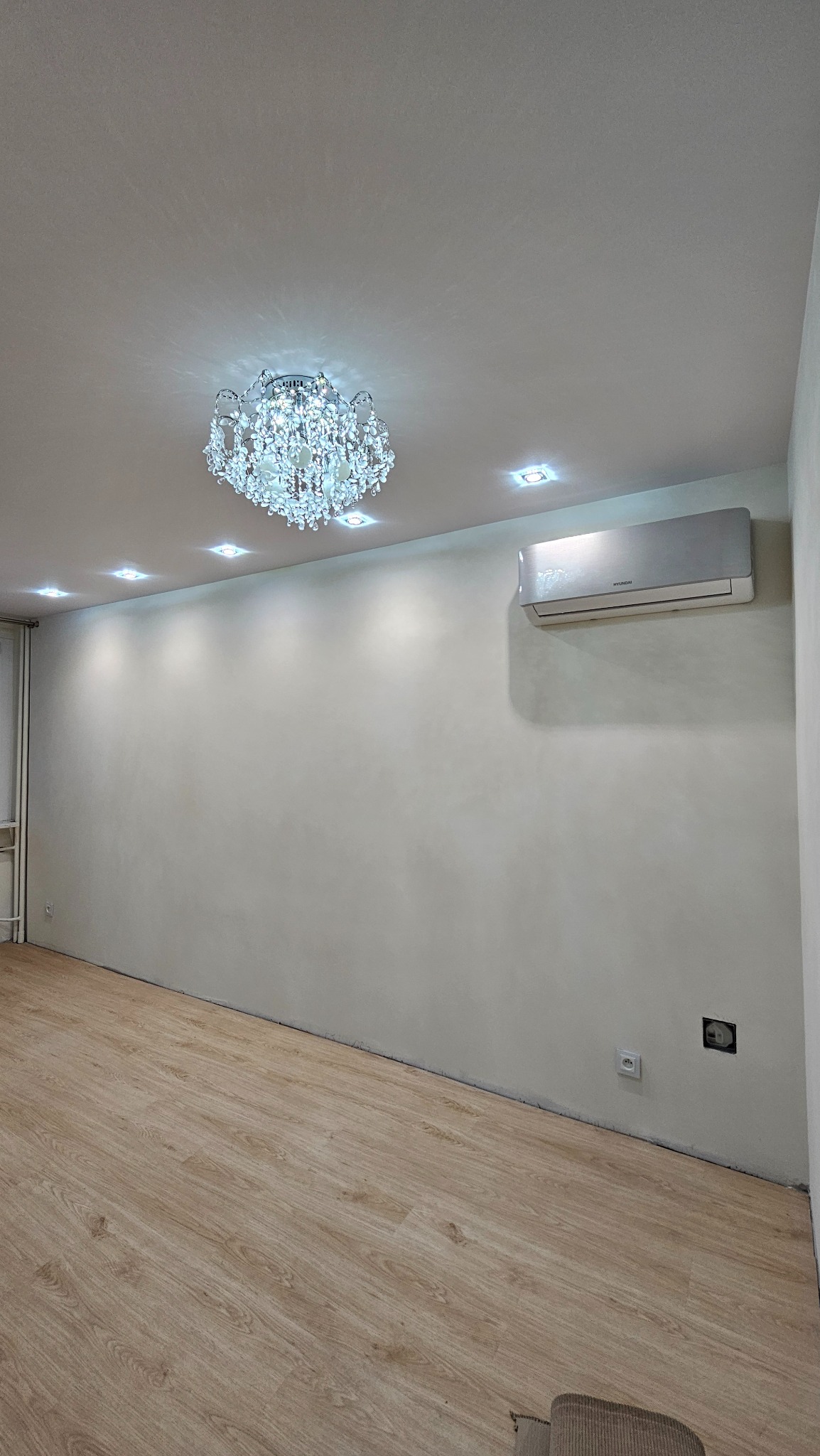 Jasne wnętrze po remoncie: parkiet, gładkie ściany, klimatyzacja, ozdobny żyrandol i oświetlenie punktowe. Widoczne gniazdka elektryczne.
