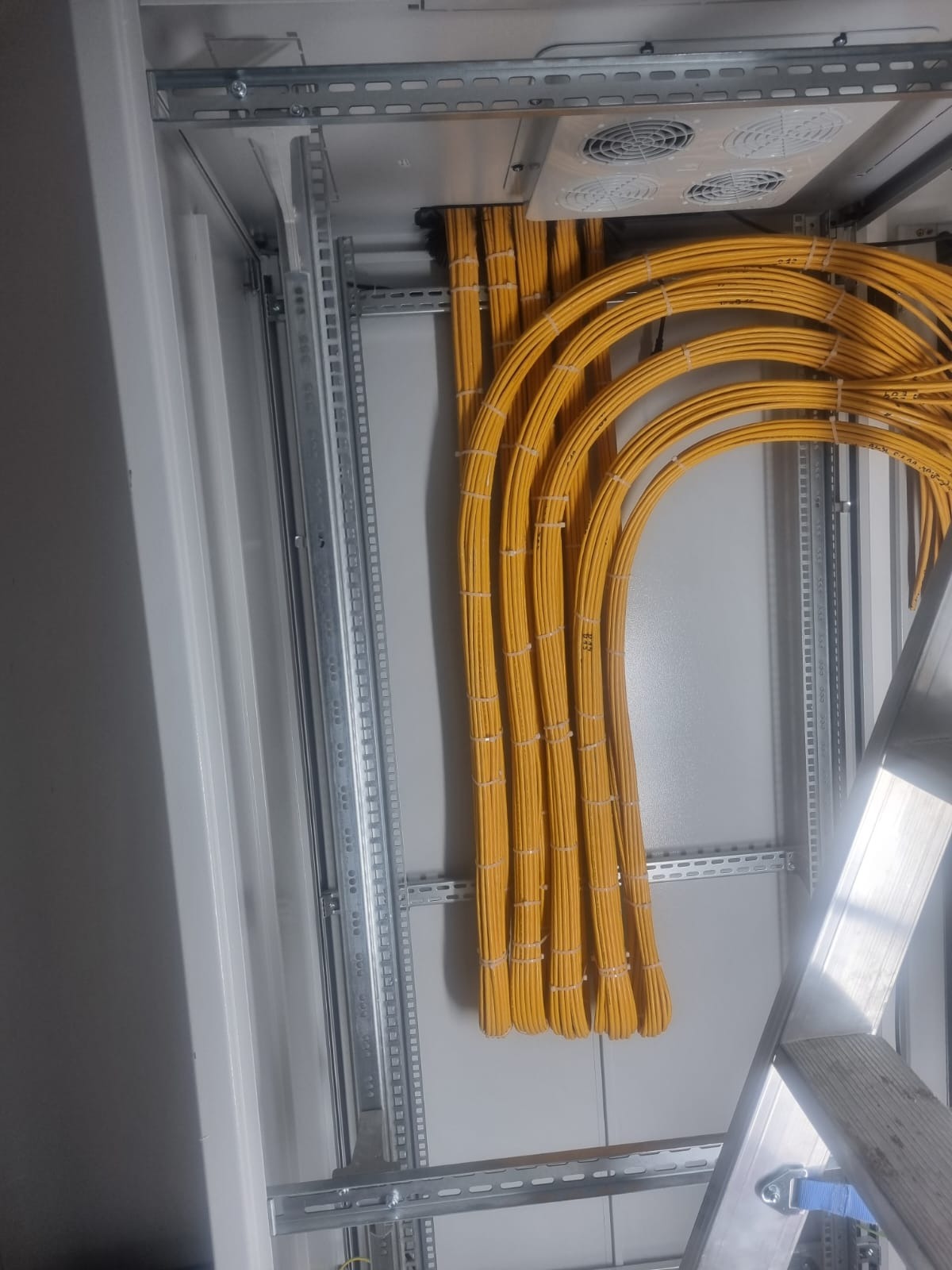 Żółte kable elektryczne uporządkowane w szafie sterowniczej, widoczne elementy montażowe i wentylator. Instalacja wykonana schludnie i profesjonalnie.