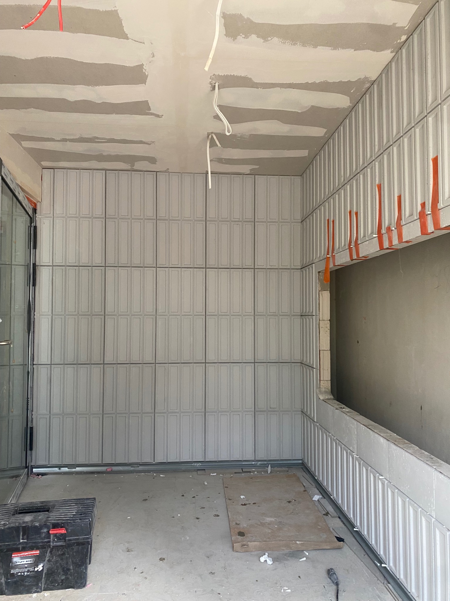 Montaż dekoracyjnych paneli ściennych w surowym wnętrzu. Widoczna skrzynka narzędziowa i przewody elektryczne. Etap prac wykończeniowych w nowym budynku.