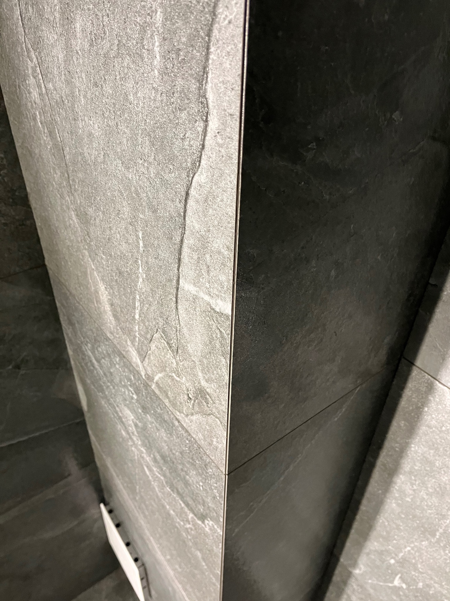 Ciemnoszara, kamieniopodobna płytka ścienna z widocznymi fugami i elementami montażowymi. Minimalistyczny design, bliski kadr.