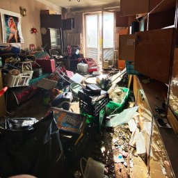 Instant Podkarpacie - Zrujnowane wnętrze mieszkania z chaotycznym nagromadzeniem przedmiotów, od mebli po sprzęt AGD, w jasnym świetle wpadającym przez balkon. Widoczny bałagan po opróżnianiu.