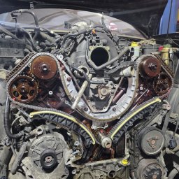 LD AUTO SERVICE MECHANIKA SAMOCHODOWA SPÓŁKA CYWILNA - Otwarty silnik samochodowy z widocznym łańcuchem rozrządu i elementami osprzętu, w trakcie naprawy w warsztacie. Widoczne ślady oleju.