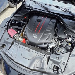 LD AUTO SERVICE MECHANIKA SAMOCHODOWA SPÓŁKA CYWILNA - Otwarta maska czarnej Toyoty Supra z widocznym silnikiem z czerwonym filtrem powietrza i elementami w kolorze czerwonym. Widoczne detale silnika i komory.