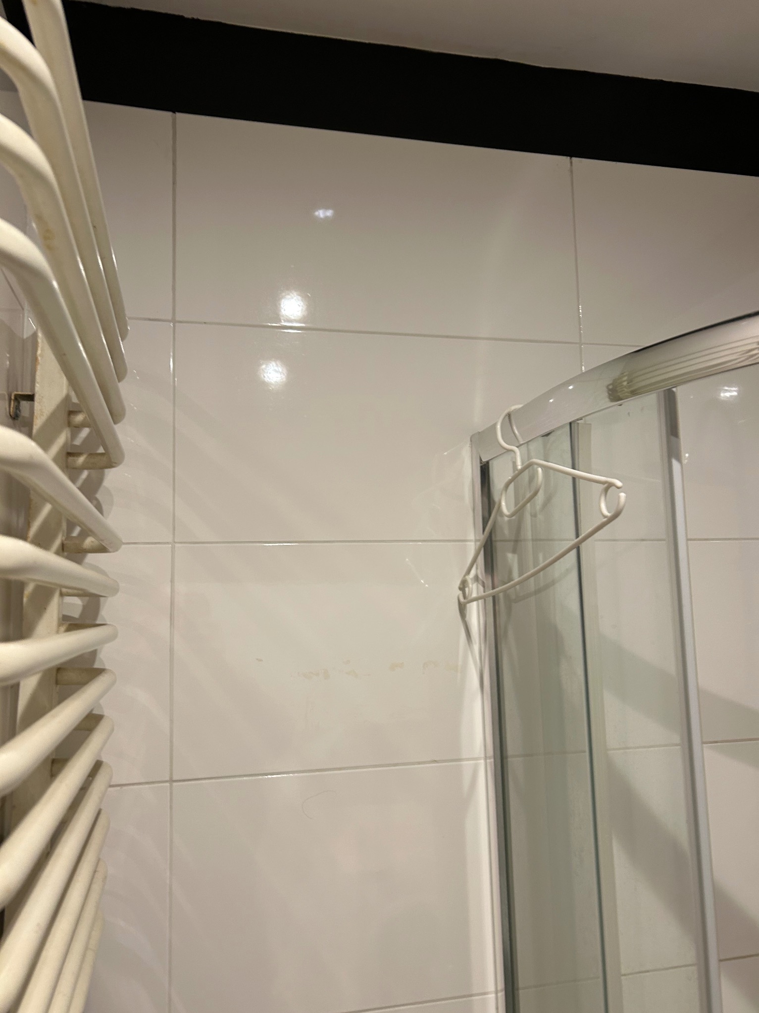 Białe płytki w łazience z grzejnikiem drabinkowym i kabiną prysznicową z wieszakiem. Minimalistyczny design, czyste linie, nowoczesne wykończenie.