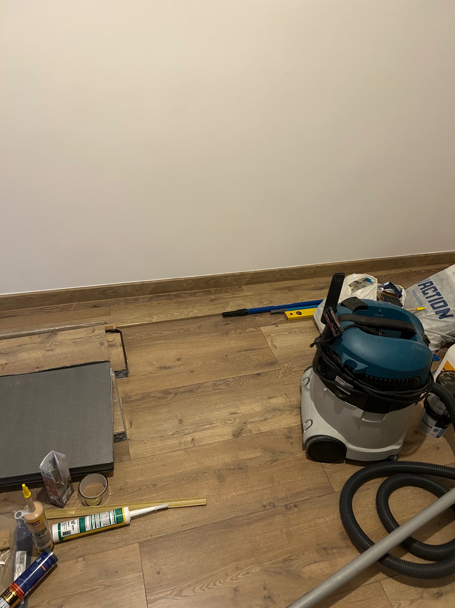 Układanie paneli podłogowych w trakcie remontu, widoczne narzędzia, odkurzacz przemysłowy i materiały budowlane na drewnianej podłodze.
