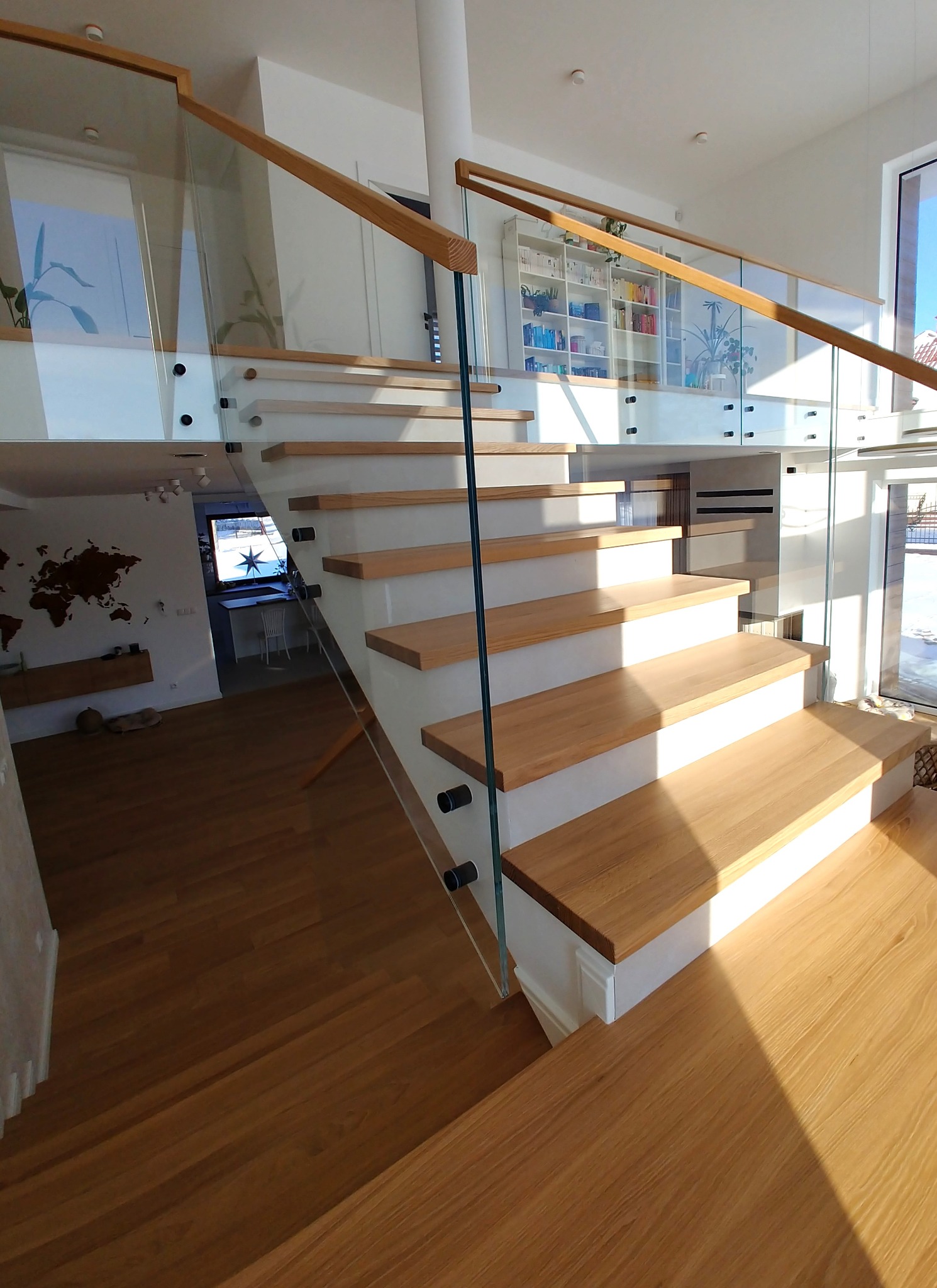 Nowoczesne schody z drewnianymi stopniami i szklaną balustradą, mocowaną punktowo. Widok z dołu, na pierwszym planie drewniana podłoga.