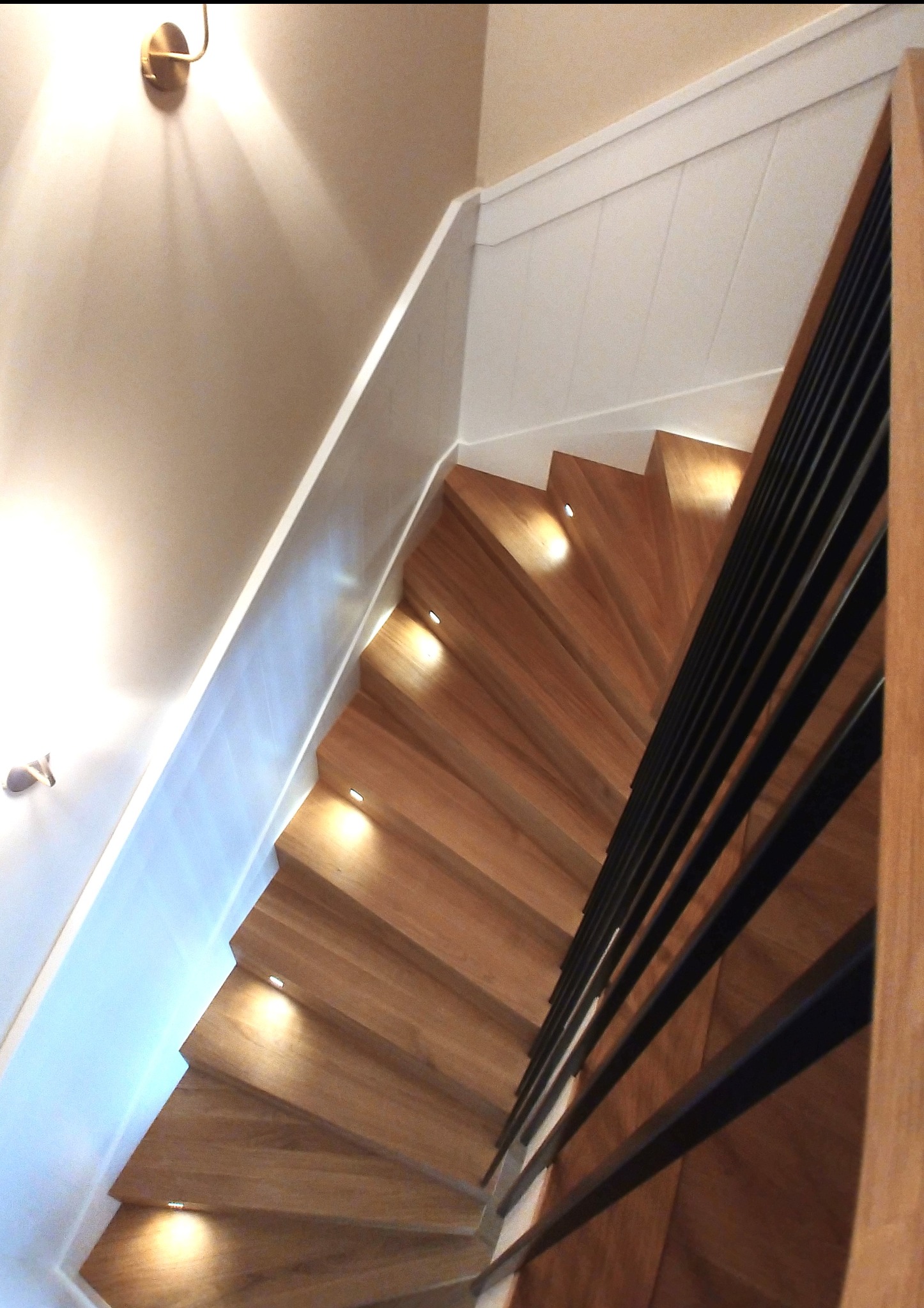 Drewniane schody z podświetleniem LED i czarną, metalową balustradą, widziane z góry. Naturalne drewno, nowoczesny design, ciepłe oświetlenie.