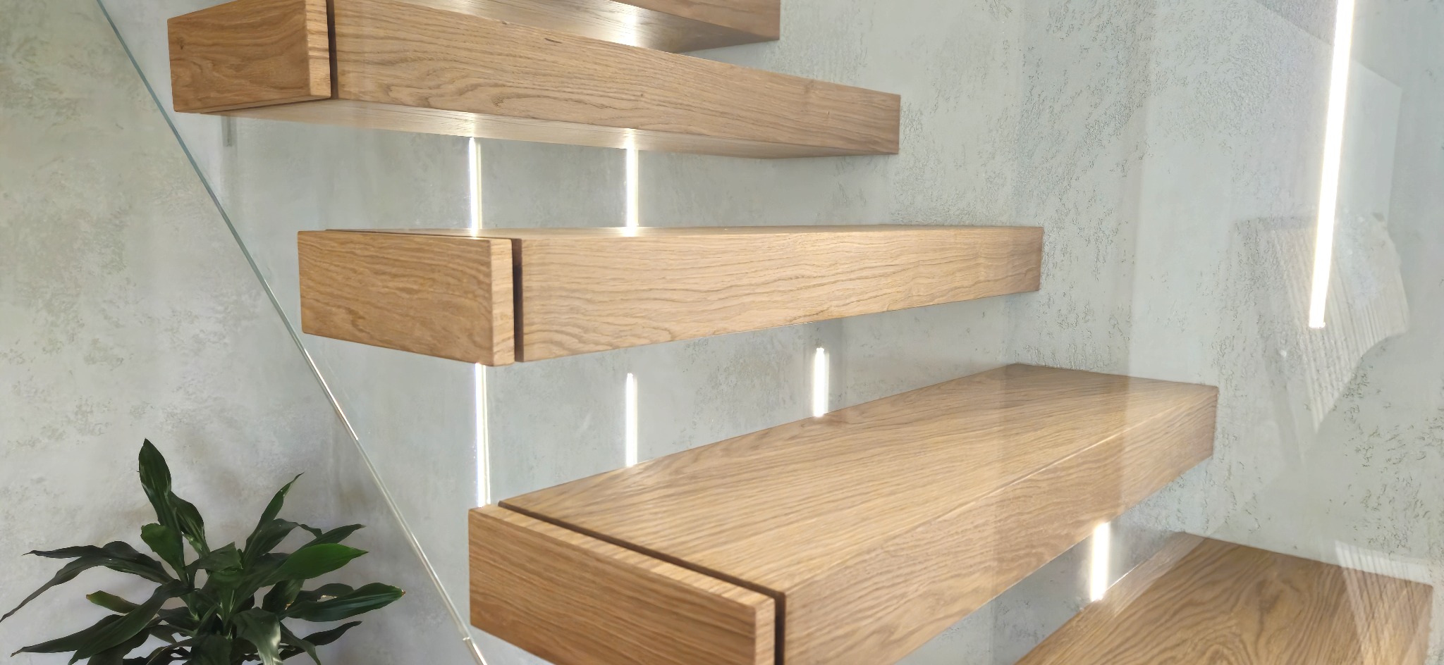 Nowoczesne, dębowe schody wiszące z podświetleniem LED i szklaną balustradą. Minimalistyczny design, jasne drewno, subtelne oświetlenie, roślina w tle.