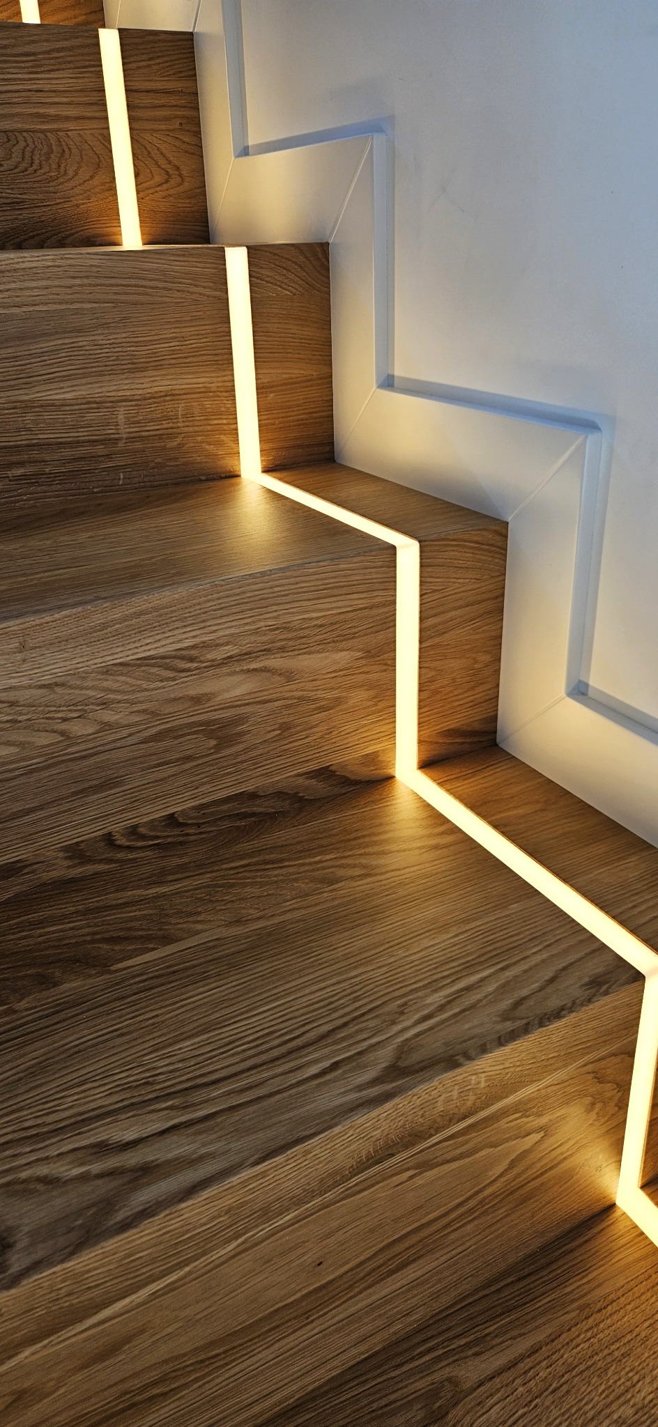 Detale drewnianych schodów z subtelnym oświetleniem LED, podkreślającym naturalny rysunek drewna i nowoczesny design. Minimalistyczne wykończenie.