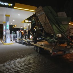 Mateusz Nowak - Transport traktora i maszyny rolniczej na niskopodwoziowej przyczepie, na tle stacji benzynowej nocą. Widoczny biały bus. Tablica rejestracyjna TK 564AP.
