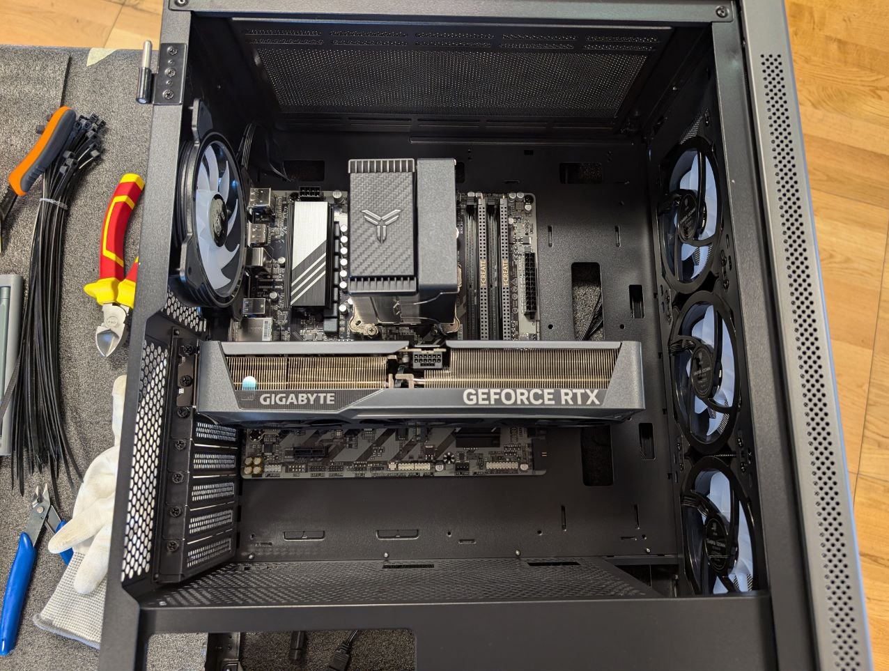 Wnętrze obudowy komputera stacjonarnego z zamontowaną kartą graficzną Gigabyte GeForce RTX, chłodzeniem procesora i wentylatorami. Widoczne narzędzia i rękawice.