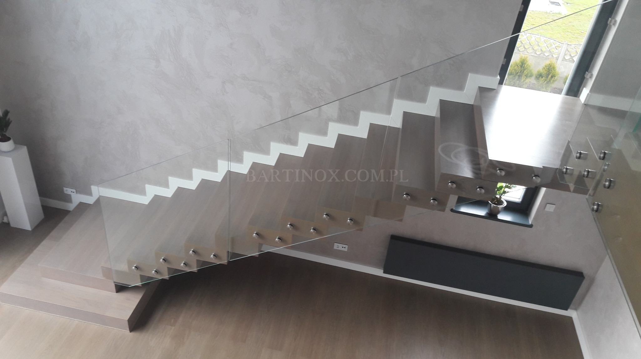 Nowoczesne schody z przezroczystą taflą szkła w Olbrachtowie. Szklana konstrukcja zamocowana na metalowych elementach. Widok z góry na drewniane stopnie.