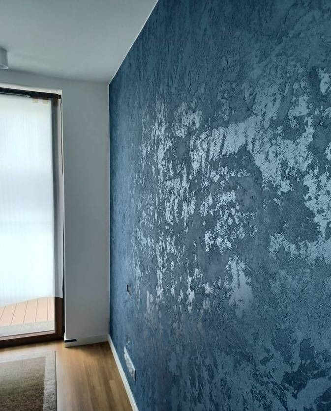 Dekoracyjna ściana w odcieniach granatu i srebra z efektem strukturalnym. Widoczny fragment okna z roletą i podłogi. Unikalna faktura ściany.