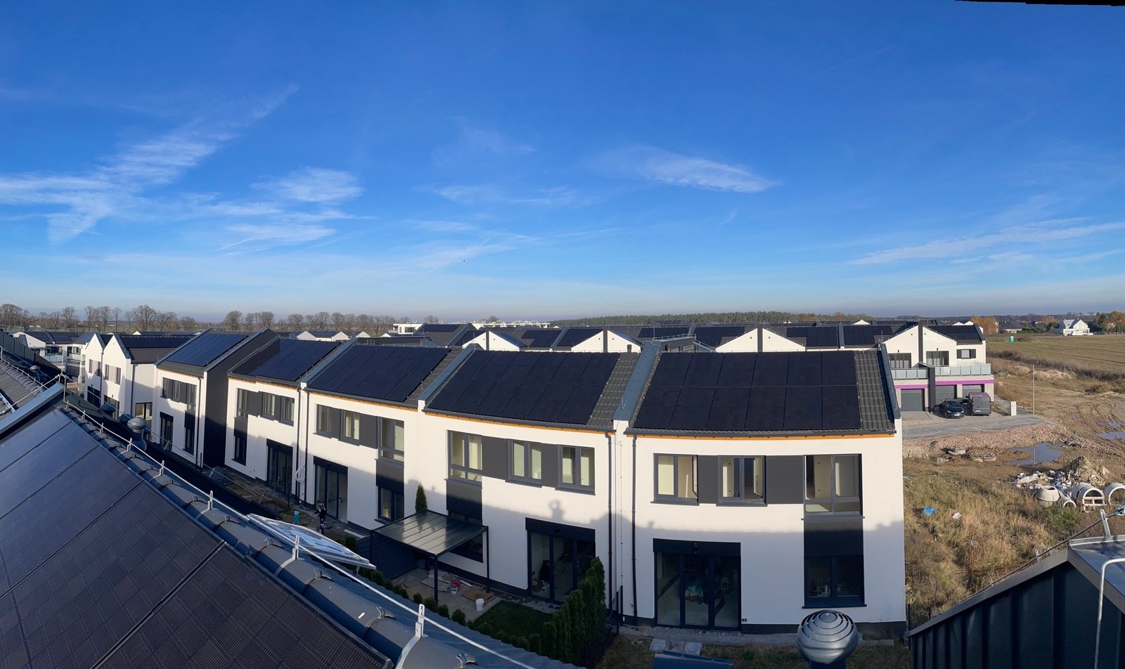 Rząd nowoczesnych domów z panelami słonecznymi na dachach, widok z góry w słoneczny dzień. Nowe osiedle z panelami fotowoltaicznymi.