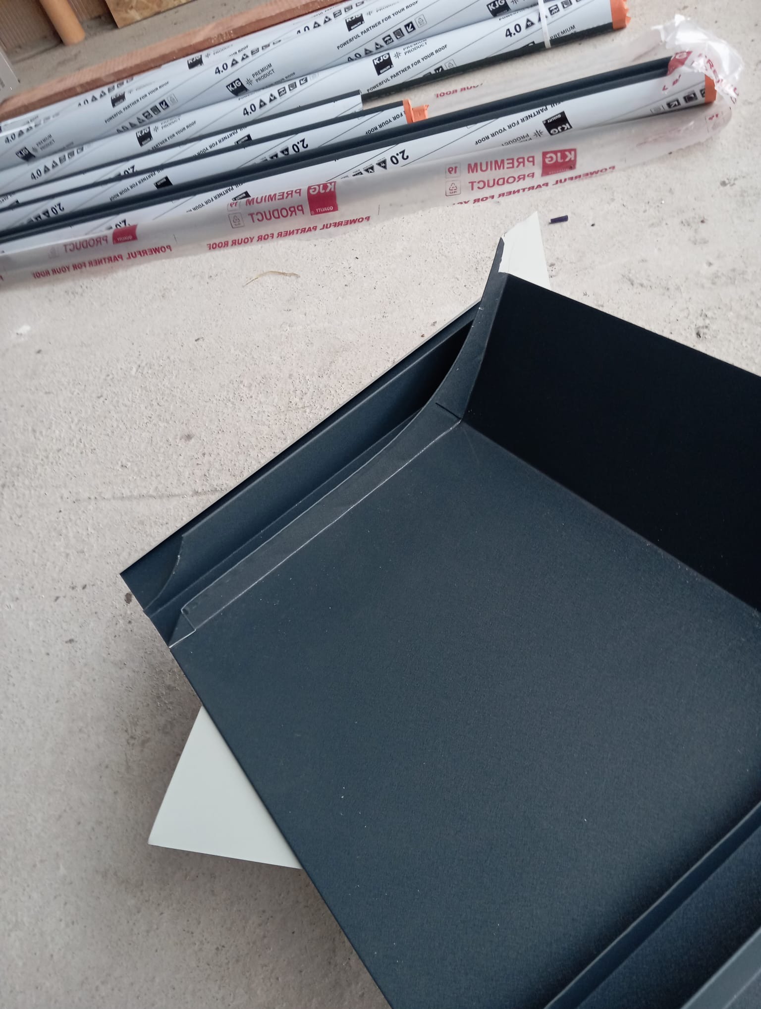 Elementy obróbki blacharskiej w kolorze grafitowym, przygotowane do montażu na dachu. W tle widoczne opakowania z profilami.