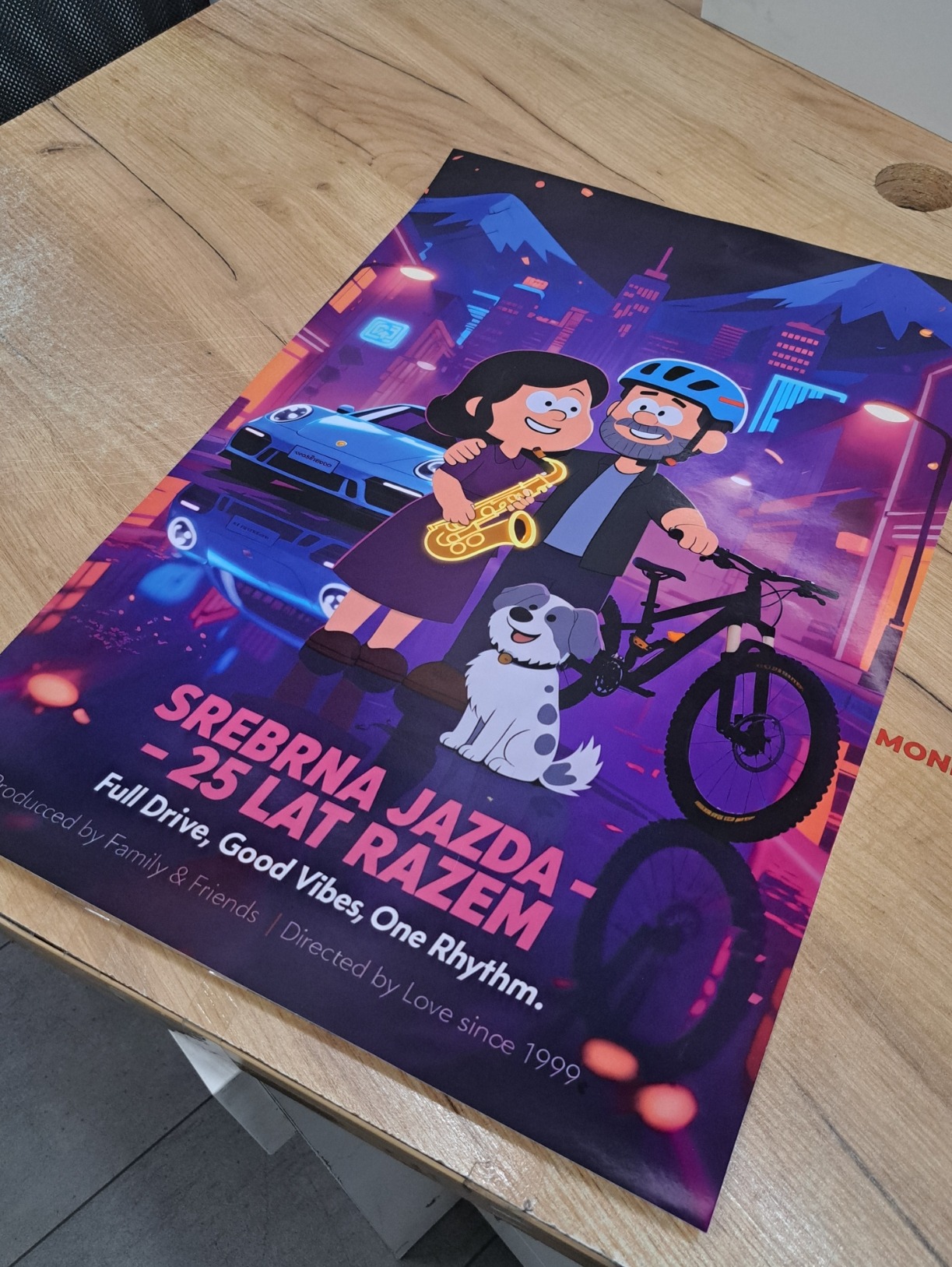 Ilustracja w stylu kreskówki na plakacie: para z psem, samochód i rower na tle miasta nocą. Napis: Srebrna Jazda - 25 lat razem. Wyraźne, nasycone kolory.