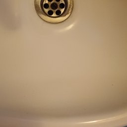 Clean & Care Heroes Marzena Dominik-Kublik - Biała umywalka z odpływem, widok z góry, fragment podłogi z butem w tle. Ujęcie na detale czystości i stanu umywalki.