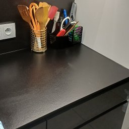 Clean & Care Heroes Marzena Dominik-Kublik - Uporządkowany blat kuchenny z przyborami w pojemnikach: drewniane łyżki, łopatki, pędzle i akcesoria biurowe. Czysta, błyszcząca powierzchnia blatu i minimalistyczny design.