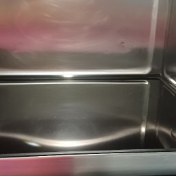 Clean & Care Heroes Marzena Dominik-Kublik - Wnętrze czystego piekarnika z oświetleniem halogenowym, widoczne odbicia na metalowej powierzchni. Panel sterowania z wyświetlaczem czasu na pierwszym planie.