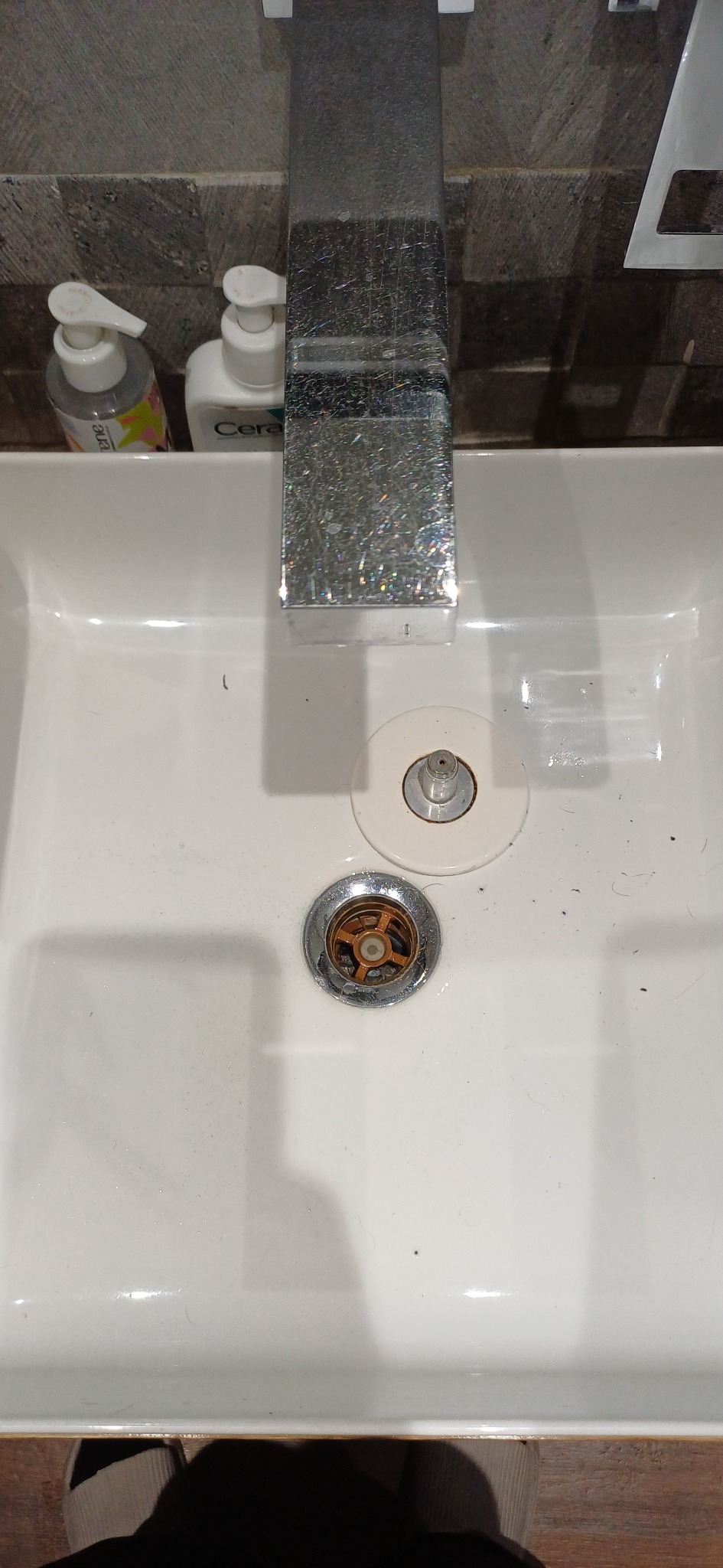 Biała umywalka z chromowaną baterią i odpływem, widok z góry. Drobne zabrudzenia widoczne w zlewie. Usługa czyszczenia łazienki w Łodzi.