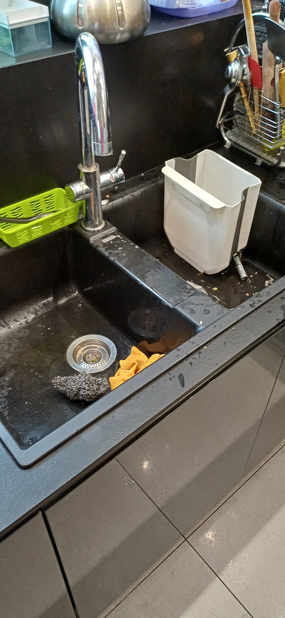 Zlew kuchenny z resztkami jedzenia, gąbką i drucianą myjką. Widoczny kran i ociekacz. Ujęcie z góry, ukazujące stan przed sprzątaniem.