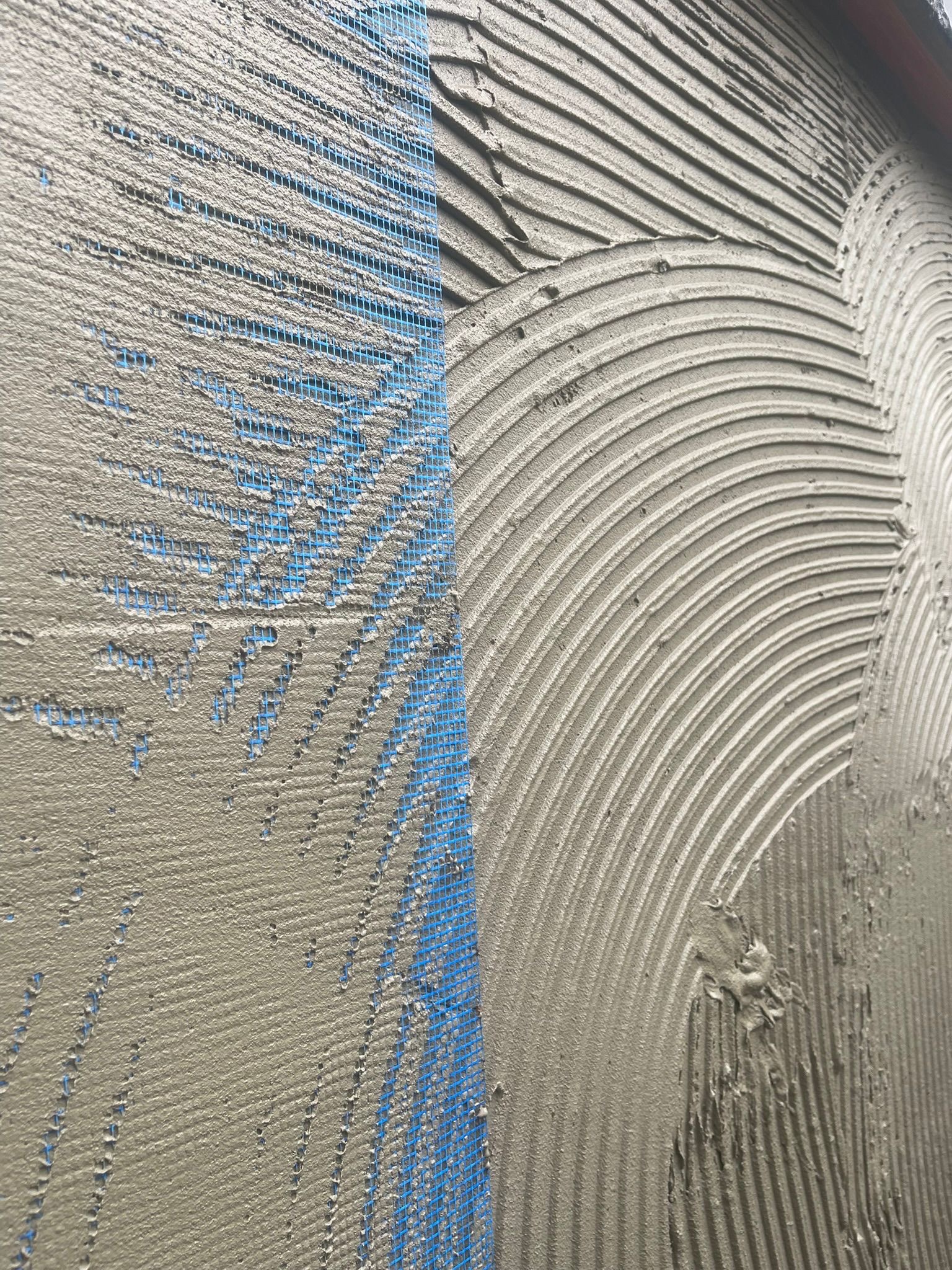 Świeżo nałożona warstwa zaprawy na elewacji z widoczną siatką wzmacniającą, przygotowana do dalszych prac wykończeniowych.