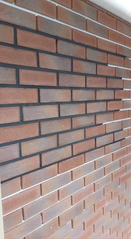 Ceglana elewacja z ciemną fugą, wykonana z klinkieru w odcieniach czerwieni i brązu. Fragment ściany z widocznymi detalami wykończenia.