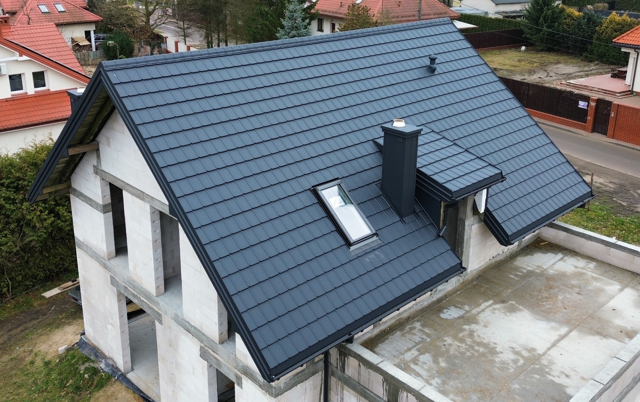 Nowoczesny, grafitowy dach z oknem połaciowym i kominem na surowym budynku z betonu komórkowego, widok z góry.