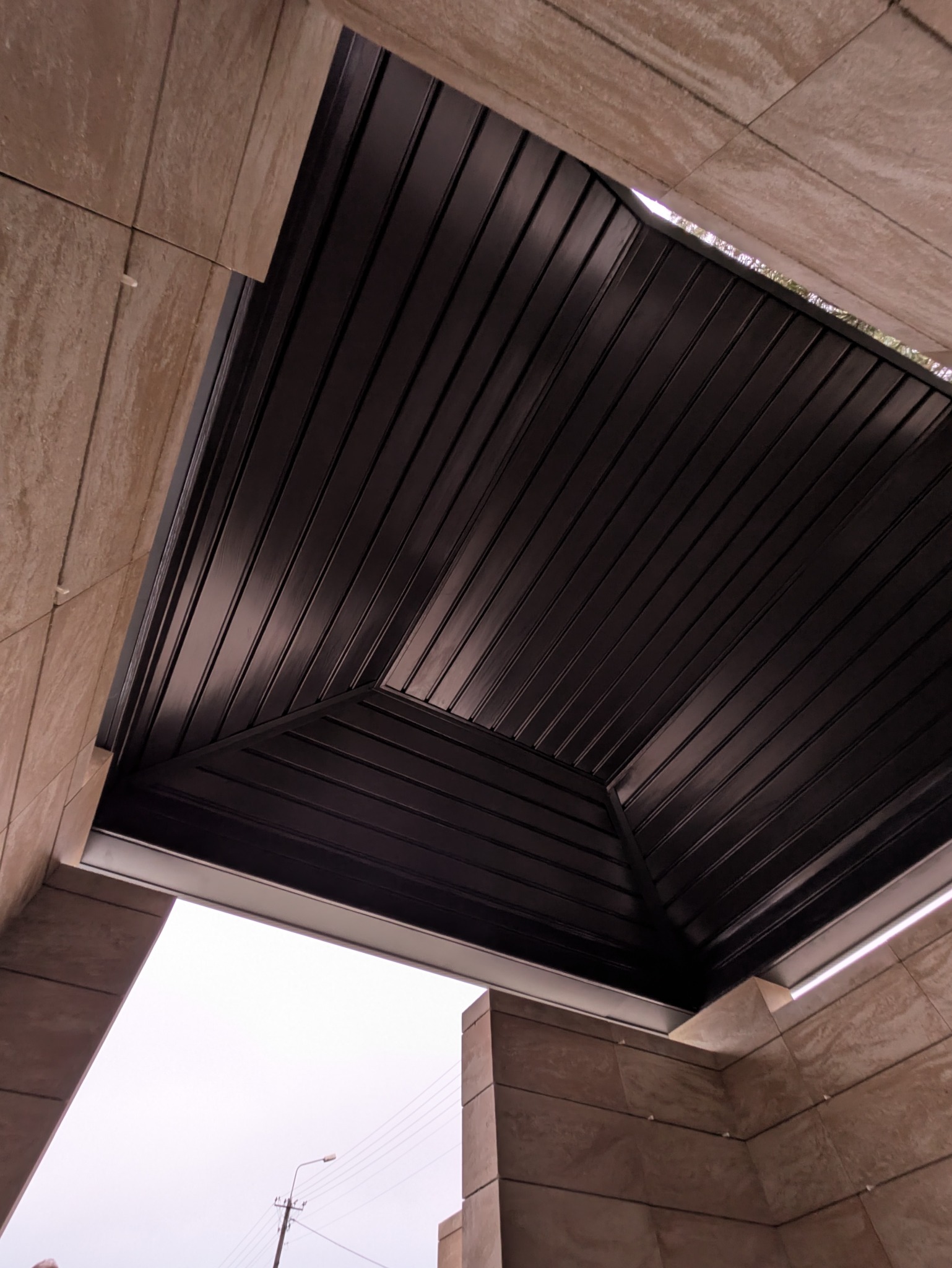 Nowoczesne zadaszenie z ciemnej blachy trapezowej, widok z dołu, z elementami wykończenia z płytek imitujących kamień. Minimalistyczny design.