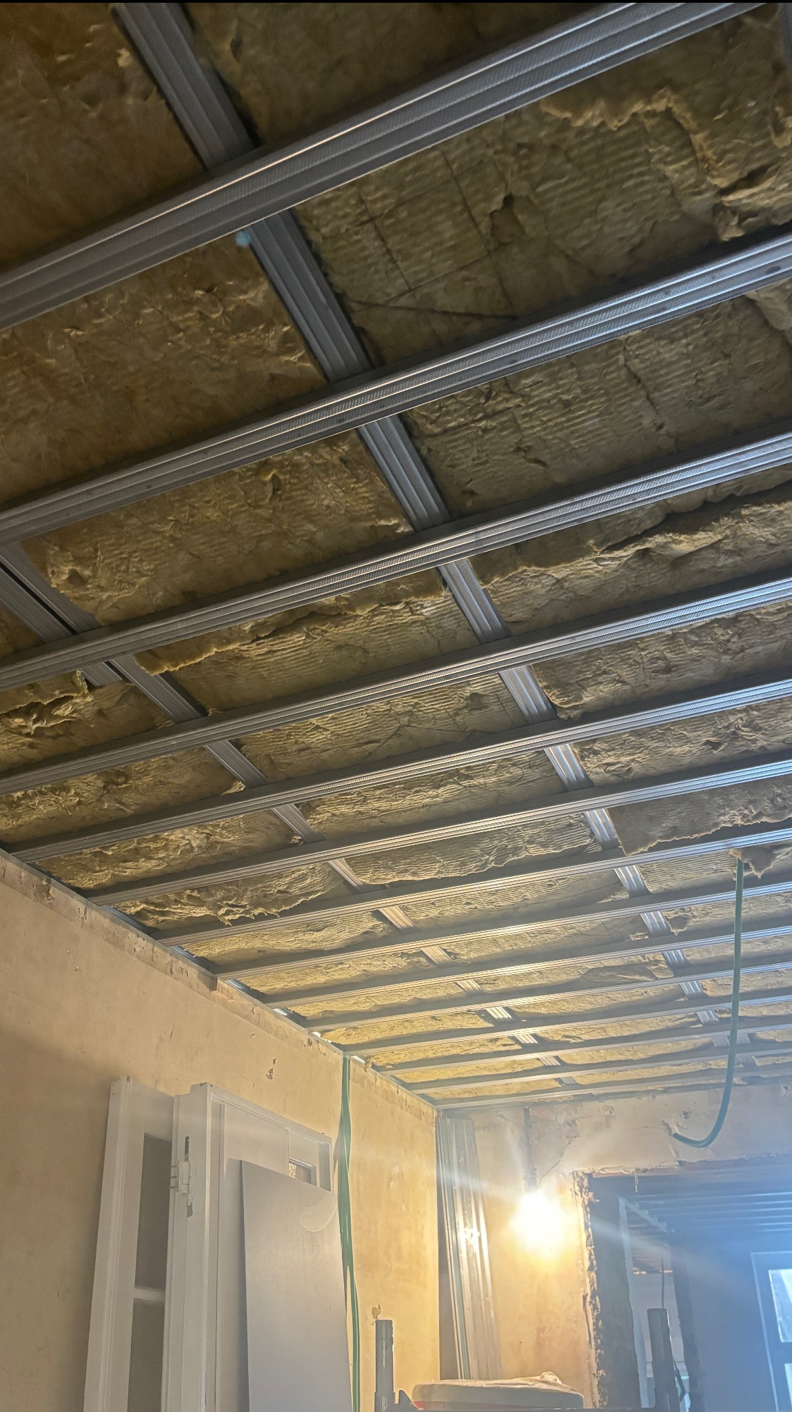 Ocieplenie poddasza wełną mineralną, widoczne metalowe profile konstrukcyjne. Prace wykończeniowe w trakcie realizacji, widoczne przewody elektryczne.