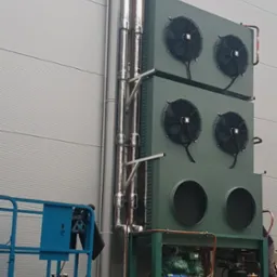 Zewnętrzna instalacja chłodnicza z trzema modułami wentylatorowymi zamontowana na metalowej konstrukcji, z widocznymi rurami chłodniczymi i elementami sprężarkowymi, umieszczona przy szarej ścianie...