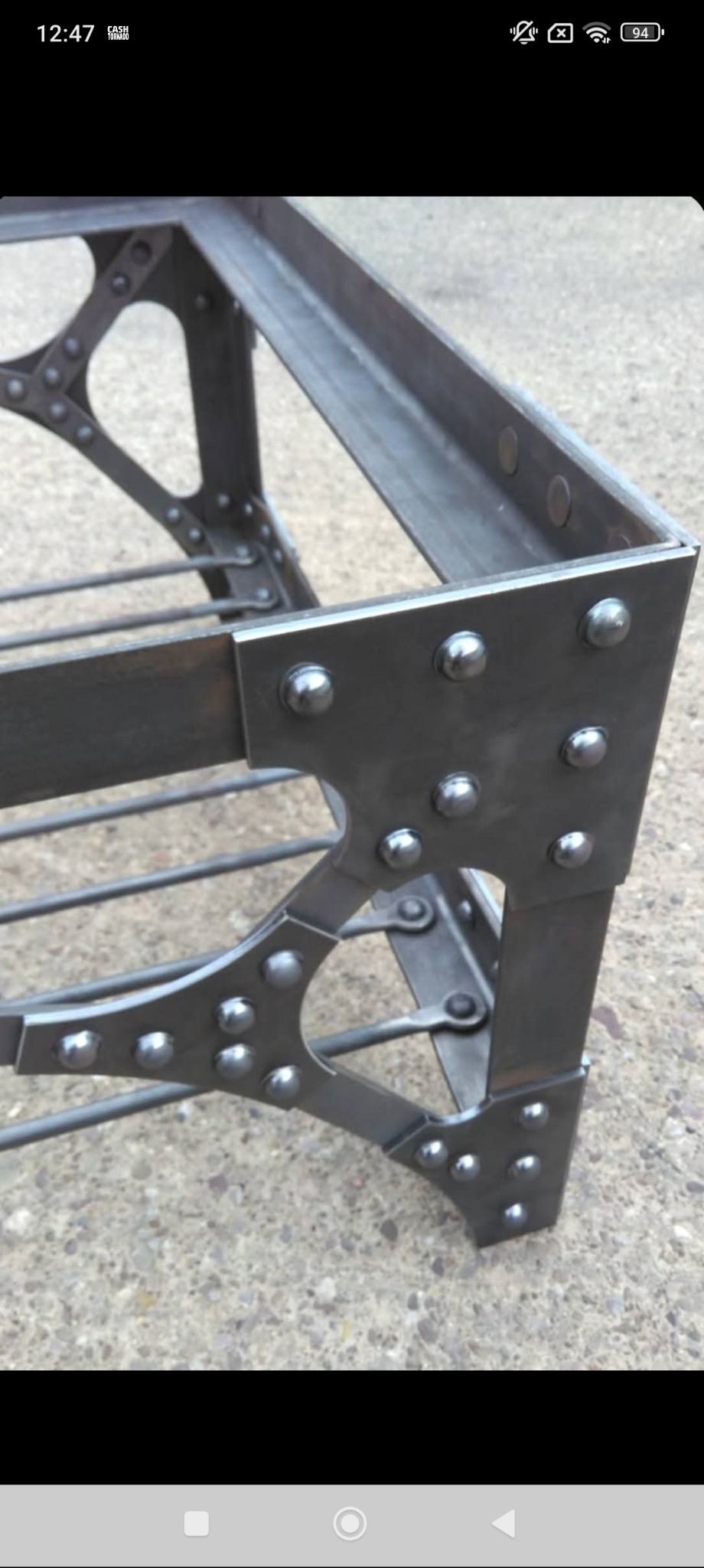 Metalowa konstrukcja spawana z nitowanymi elementami, widoczne spawy i łączenia, surowy industrialny styl, szara kolorystyka, zbliżenie na detal.