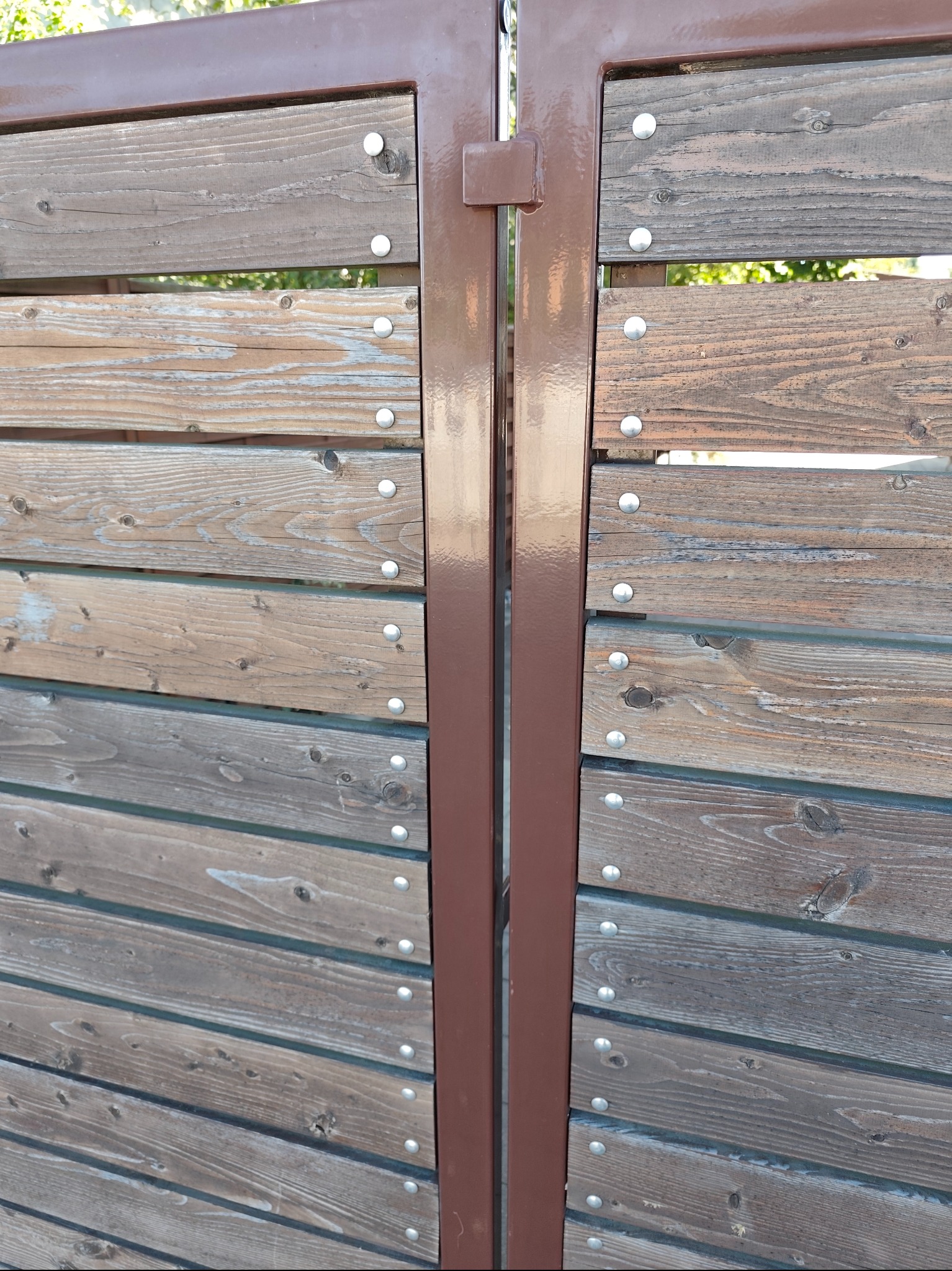 Drewniana brama z metalową ramą w kolorze brązowym, poziome deski z widocznymi śrubami, naturalne usłojenie drewna, widok z bliska.