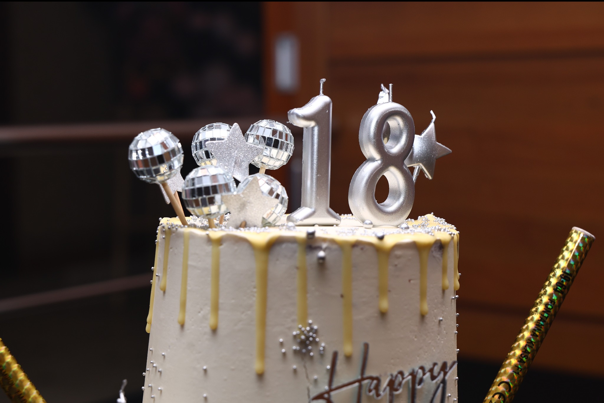 Tort urodzinowy z dekoracjami: srebrne świeczki '18', mini-kule dyskotekowe i złote fontanny. Kremowy lukier i srebrne koraliki dodają elegancji. Idealny na osiemnastkę.