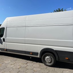 Błażej Klimczak - Biały, dostawczy bus marki Fiat Ducato, zaparkowany na brukowanej nawierzchni, z widocznymi detalami karoserii i opon. Błękitne niebo w tle.