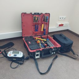 ZELITE Pomiary Projekty elektryczne - Otwarta skrzynka narzędziowa z miernikiem elektrycznym Kewtech KT63DL na podłodze, obok gniazd elektrycznych. Widoczne śrubokręty i inne narzędzia.