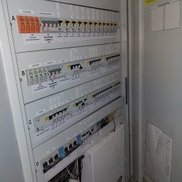 ZELITE Pomiary Projekty elektryczne - Otwarta szafa elektryczna z bezpiecznikami, wyłącznikami i schematami. Widoczne oznaczenia i przewody. Solid Security na dole.