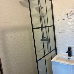 Ivan Vovk - Nowoczesna kabina prysznicowa z czarnymi profilami na tle białych, trójwymiarowych płytek. Umywalka z czarną armaturą. Minimalistyczny design łazienki.