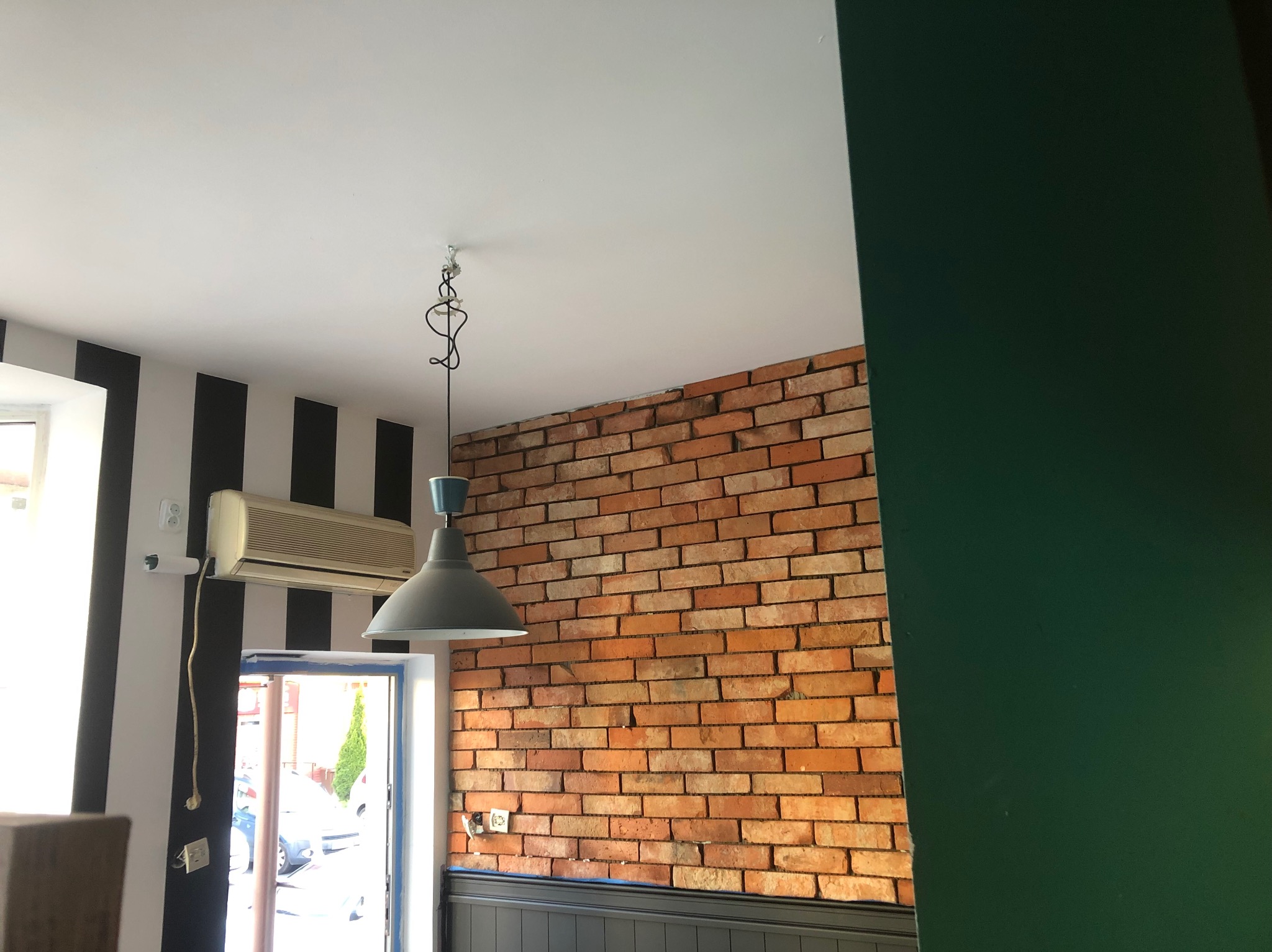 Ceglana ściana z szarą lampą wiszącą, klimatyzator na ścianie w czarno-białe pasy. Widok na wnętrze z elementami wykończenia.