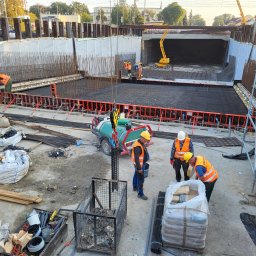 Hydrostop - Hydroizolacje krystalizujące - Budowa fundamentów pod wiadukt: zbrojenie, szalunki, pracownicy w kaskach i kamizelkach odblaskowych. Żuraw na budowie. Widok z góry na plac budowy.
