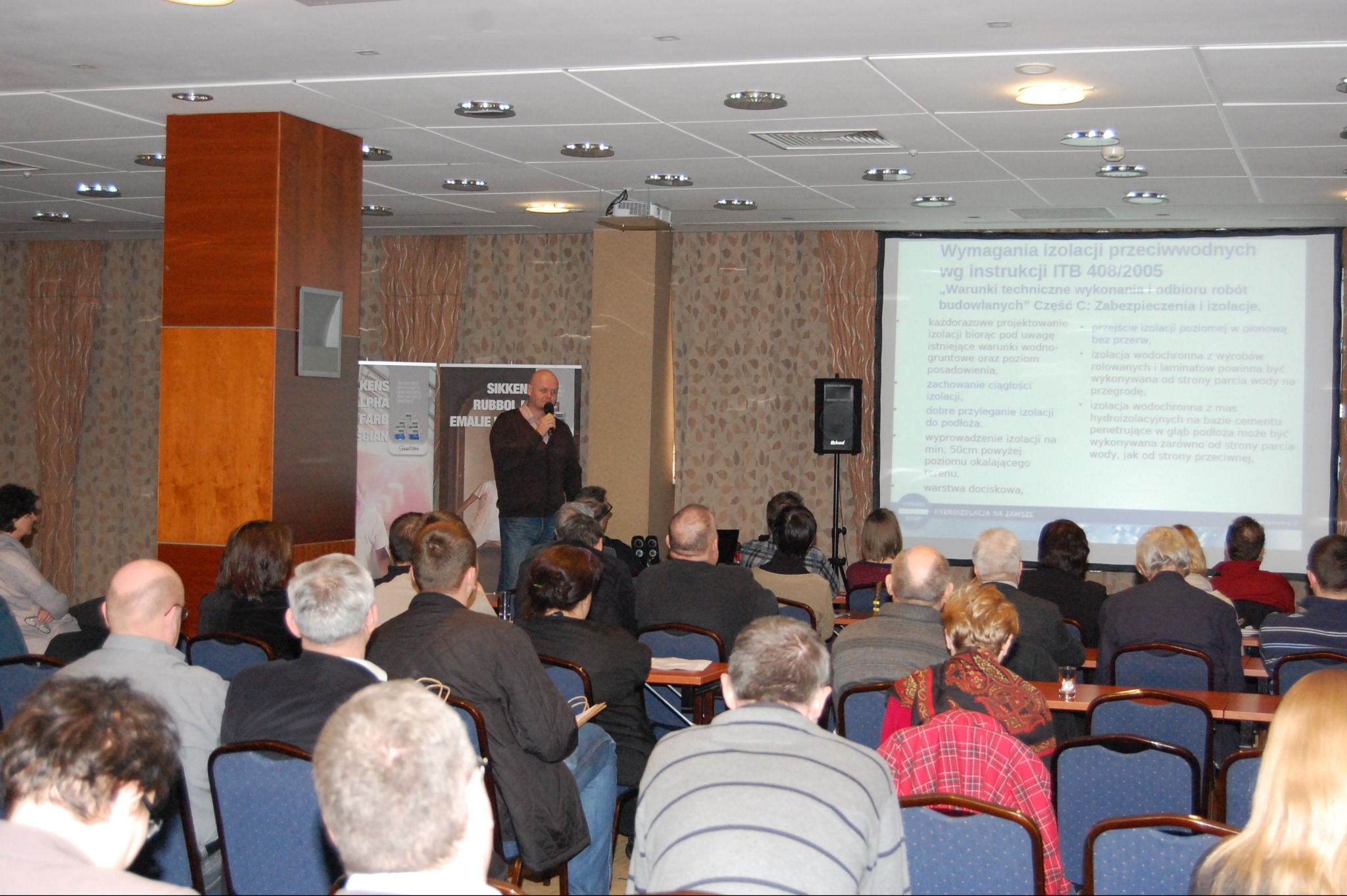 Prezentacja o izolacji przeciwwodnej fundamentów podczas konferencji. Sala wypełniona uczestnikami, na ekranie wyświetlane wymagania ITB.