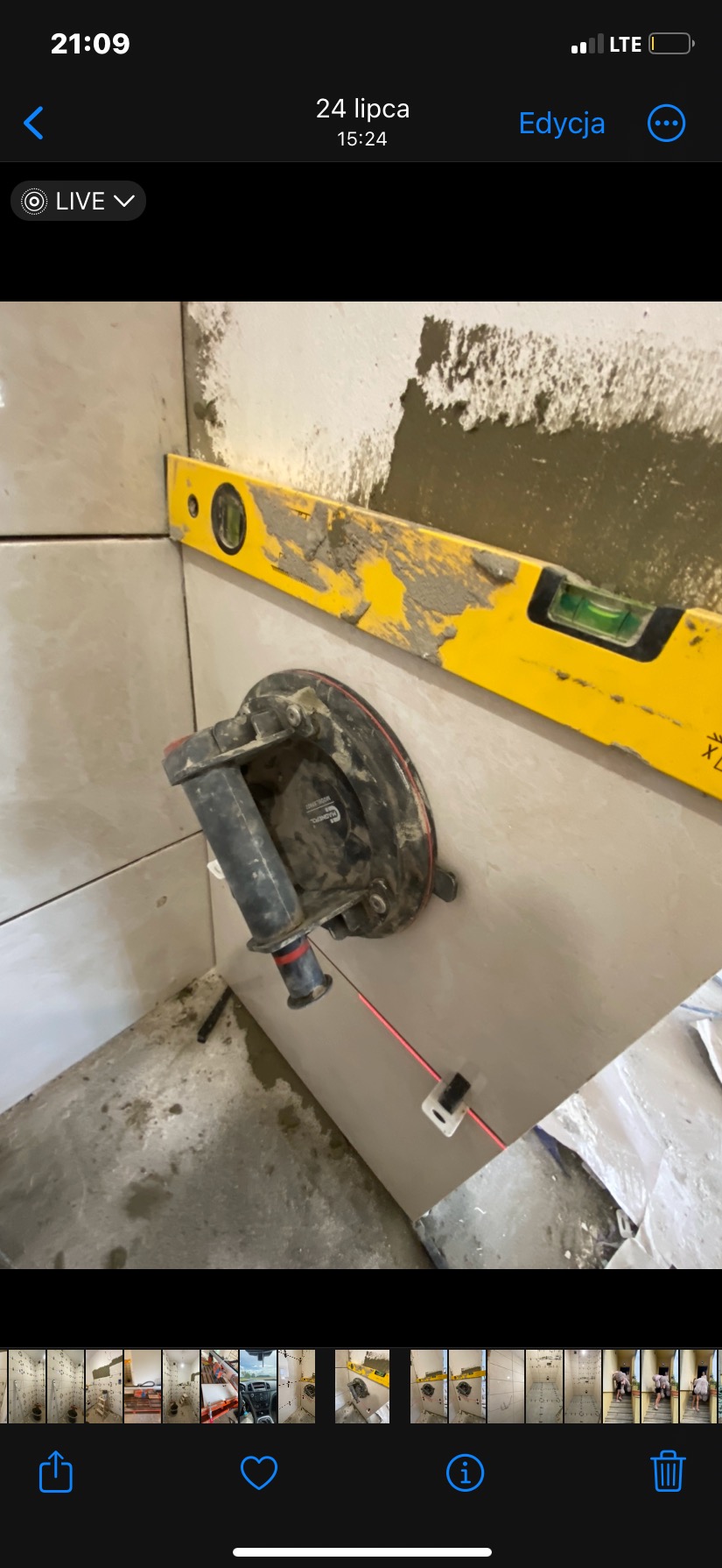 Układanie płytek w rogu łazienki. Żółta poziomica i przyssawka do płytek pomagają w precyzyjnym montażu. Widoczne zaplecze budowlane.