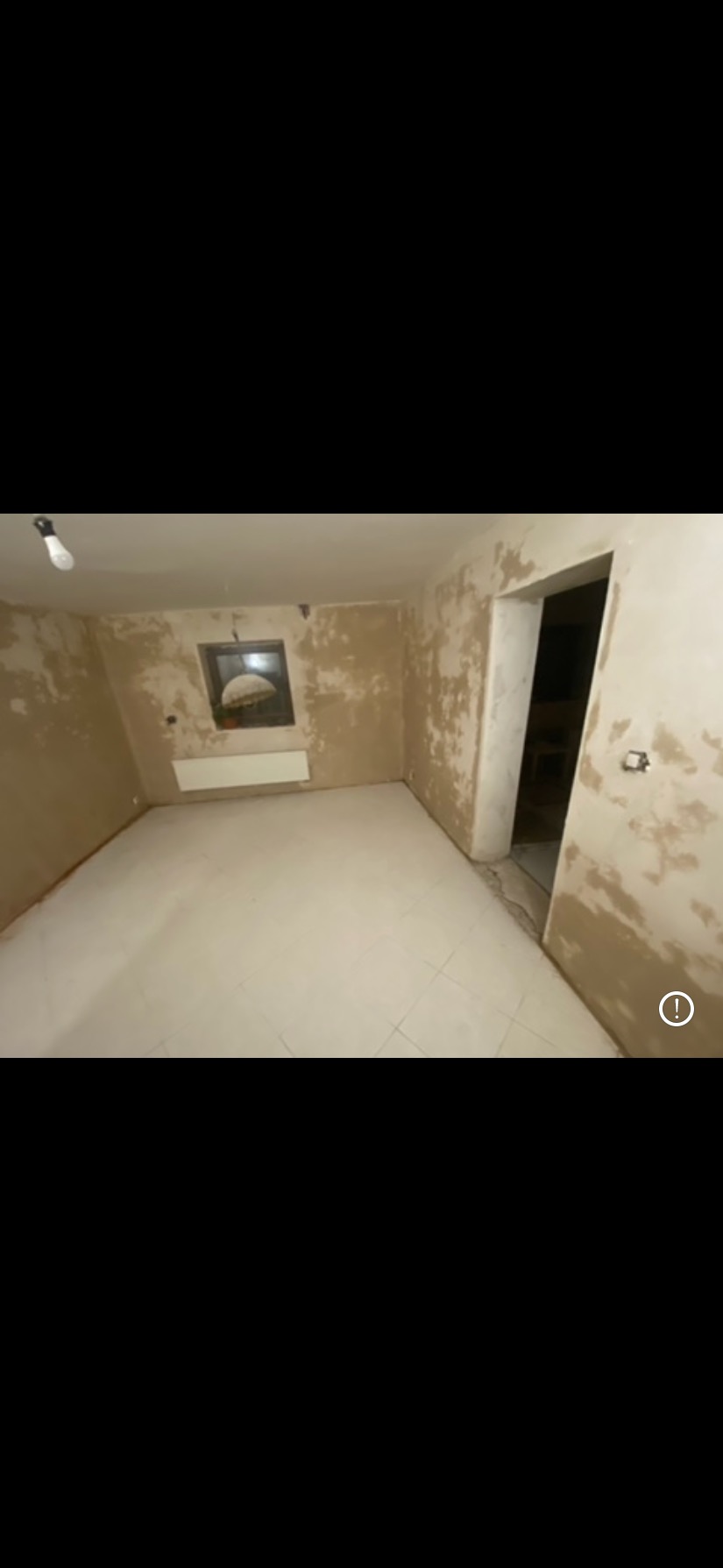 Pokój w trakcie szpachlowania w Kostomłotach. Ściany przygotowane do malowania, widoczne nierówności i gładzie. Podłoga wyłożona jasnymi płytkami.