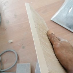 Adrian Żukowski - Nakładanie szpachli na płytę gipsową przez pracownika z opatrunkiem na palcu, widoczne narzędzia i fragment podłogi. Praca w trakcie realizacji.