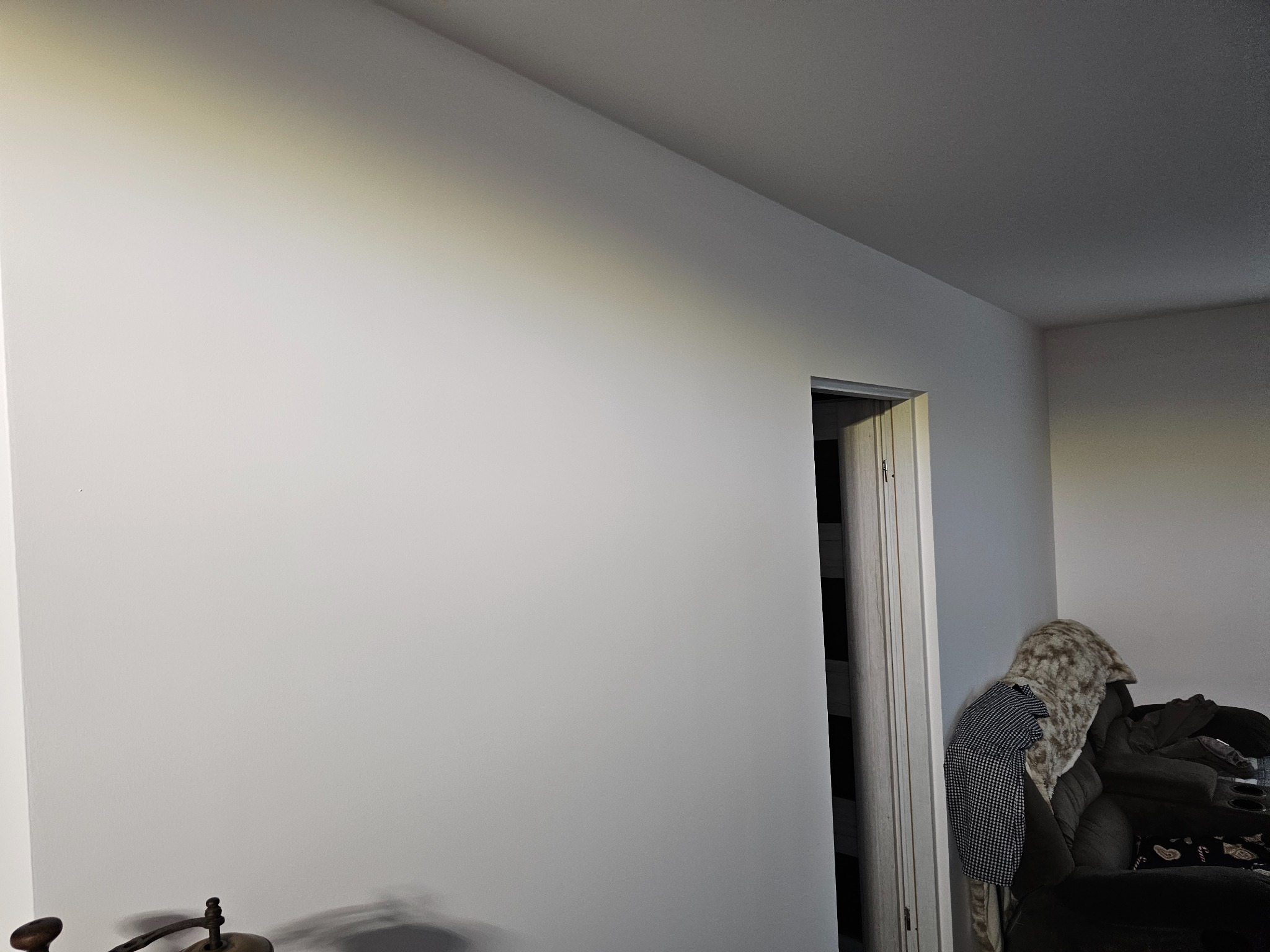Świeżo pomalowana, gładka, biała ściana w pokoju, widoczny fragment drzwi i mebli w tle. Minimalistyczne wnętrze po malowaniu.