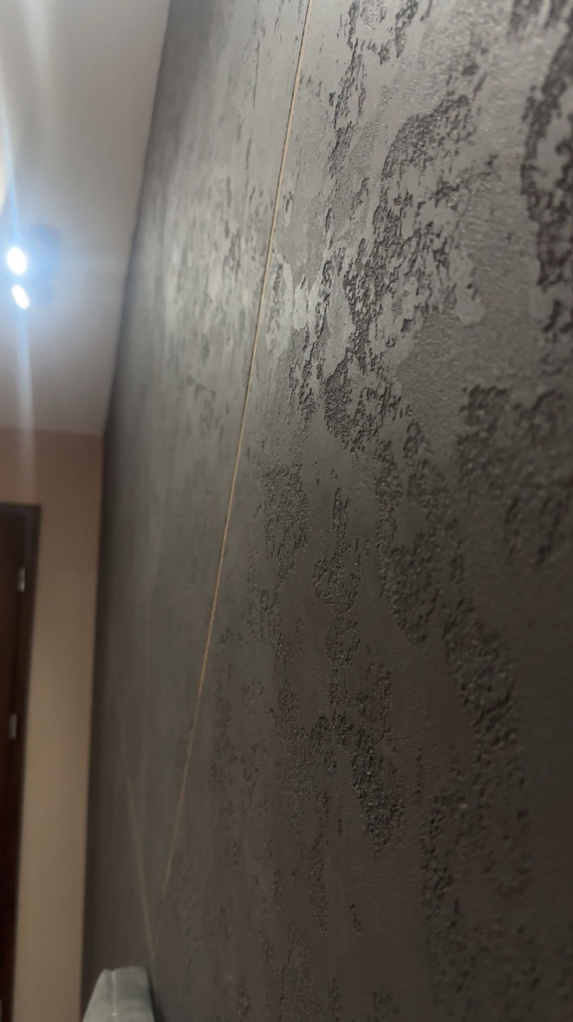 Dekoracyjna ściana z efektem strukturalnym w odcieniach szarości, z widocznym pionowym łączeniem płyt. Ujęcie z boku, podkreślające fakturę i głębię.