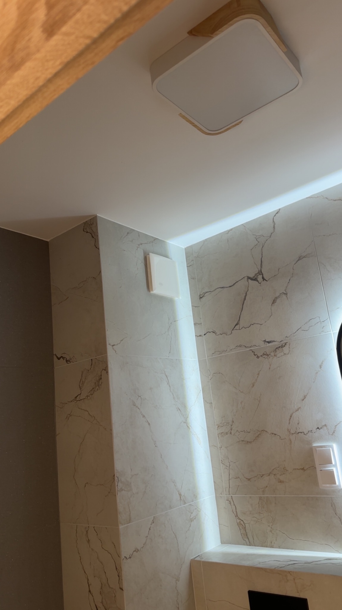 Wykończona łazienka z marmurowymi płytkami, nowoczesnym oświetleniem sufitowym i wentylatorem. Minimalistyczny design, jasne kolory, czyste linie.