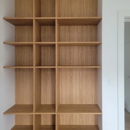 ZPHU Budziński&Motyka s.c. - Półki z jasnego drewna wnękowe, minimalistyczny design. Widoczne detale wykończenia i naturalna tekstura drewna. Białe ściany i fragment drzwi w tle.