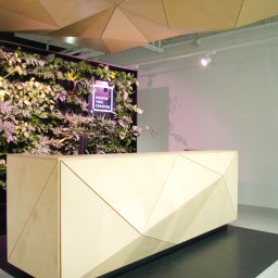 ZPHU Budziński&Motyka s.c. - Nowoczesna recepcja z drewna z geometrycznym wzorem, podświetlona ściana z roślin i designerski sufit z trójkątnych paneli. Minimalistyczne wnętrze.